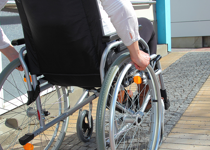 Man in a wheelchair is manually wheeling himself up a path.